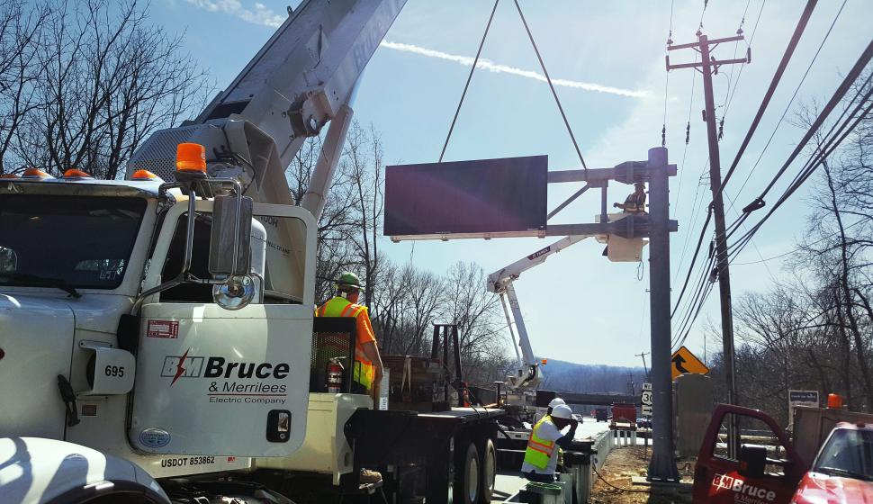 Highway construction crane setting Dynamic Message Sign (DMS) onto crossarm